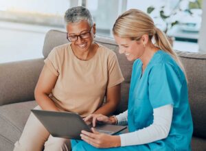 An adult child is sitting with an elderly parent in a cozy assisted living room, talking and holding hands.